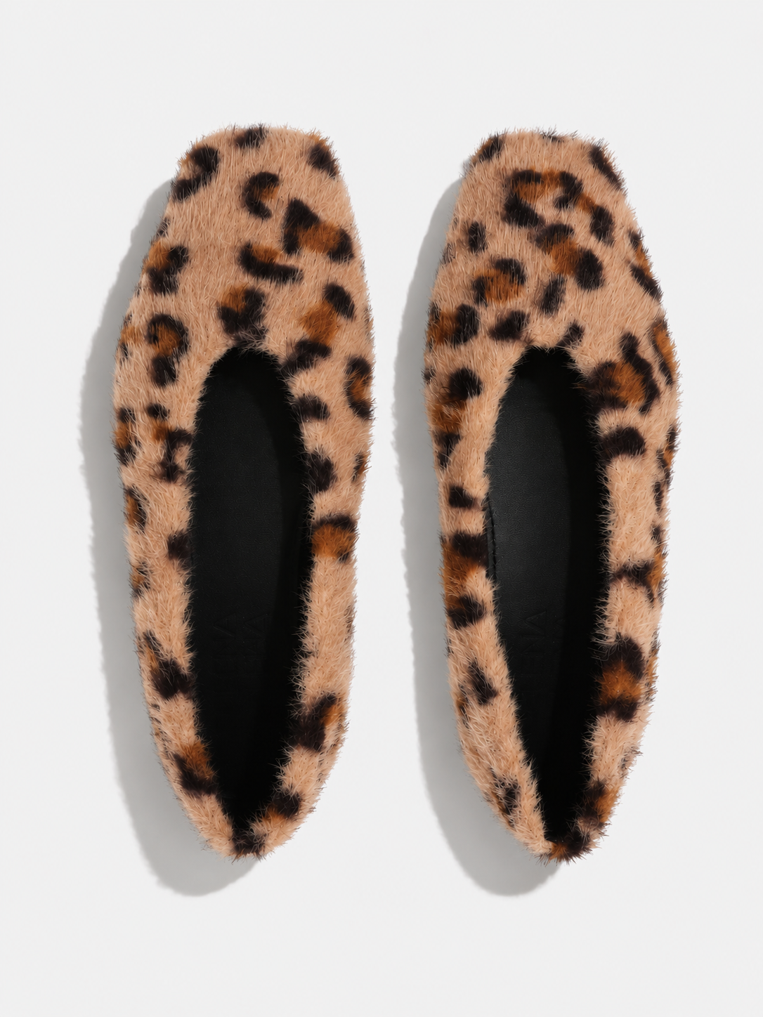 A pair of fuzzy leopard-print slip-on slippers shown from a top-down view on a light gray background.